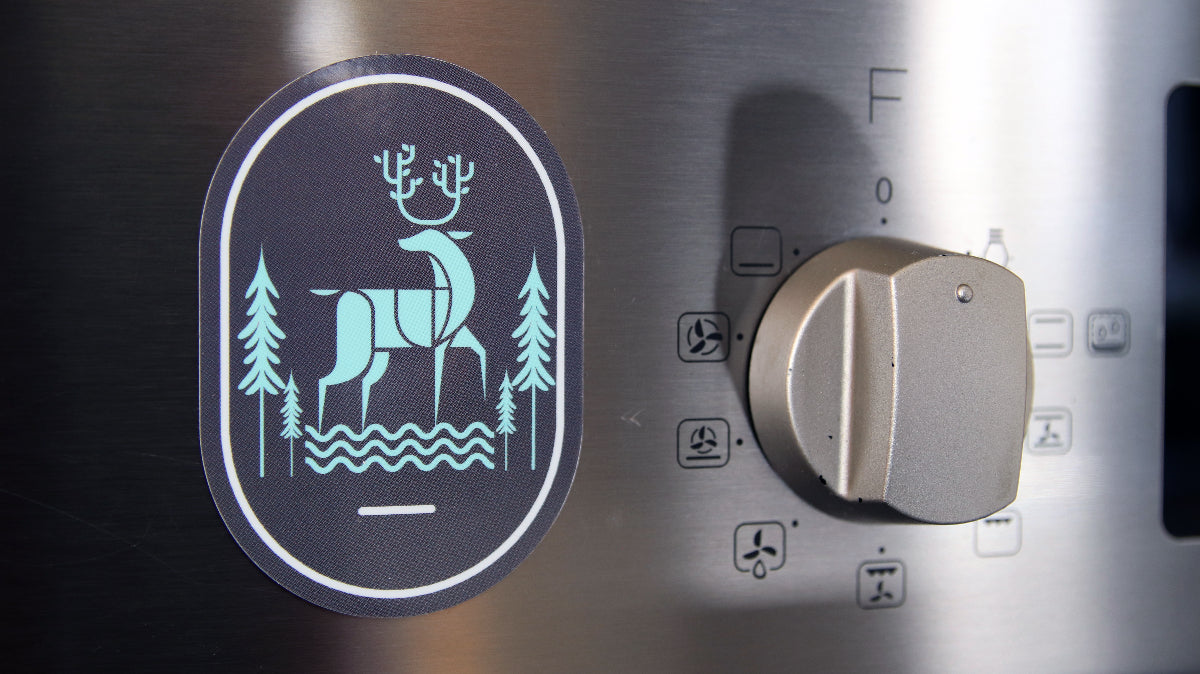 Oval magnet with a grey and light blue design stuck to an oven