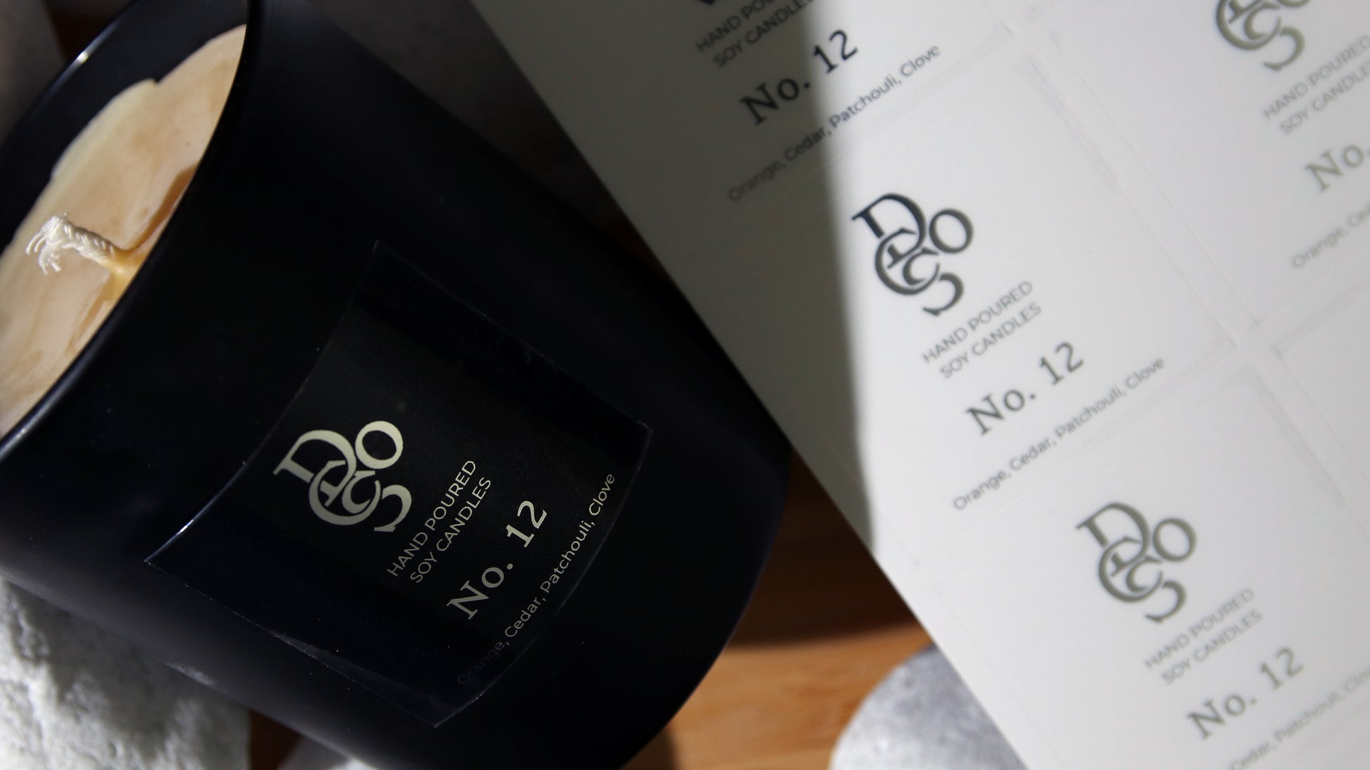 Square eco-friendly silver foil label applied to a black candle jar next to sheets of labels