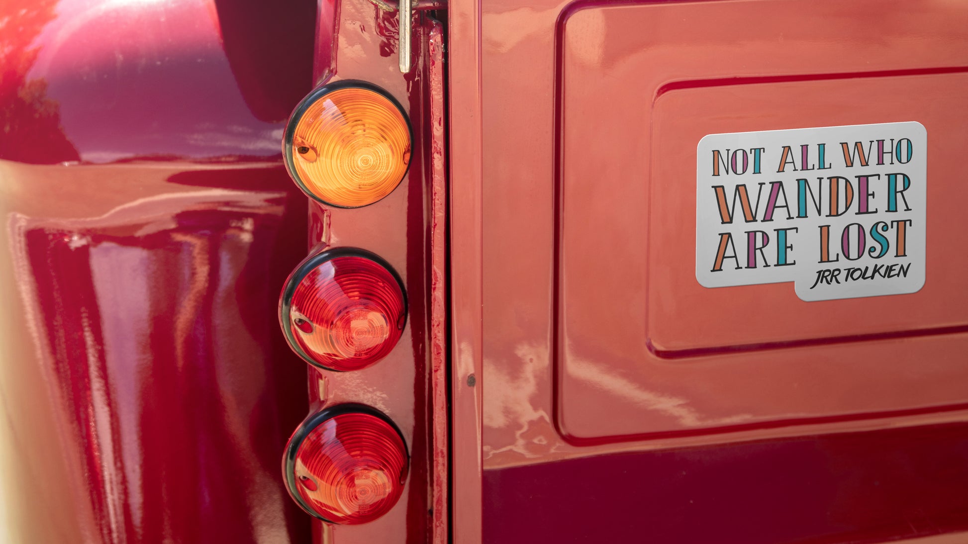 Die cut bumper sticker printed on white vinyl with wanderlust design applied to a red bumper