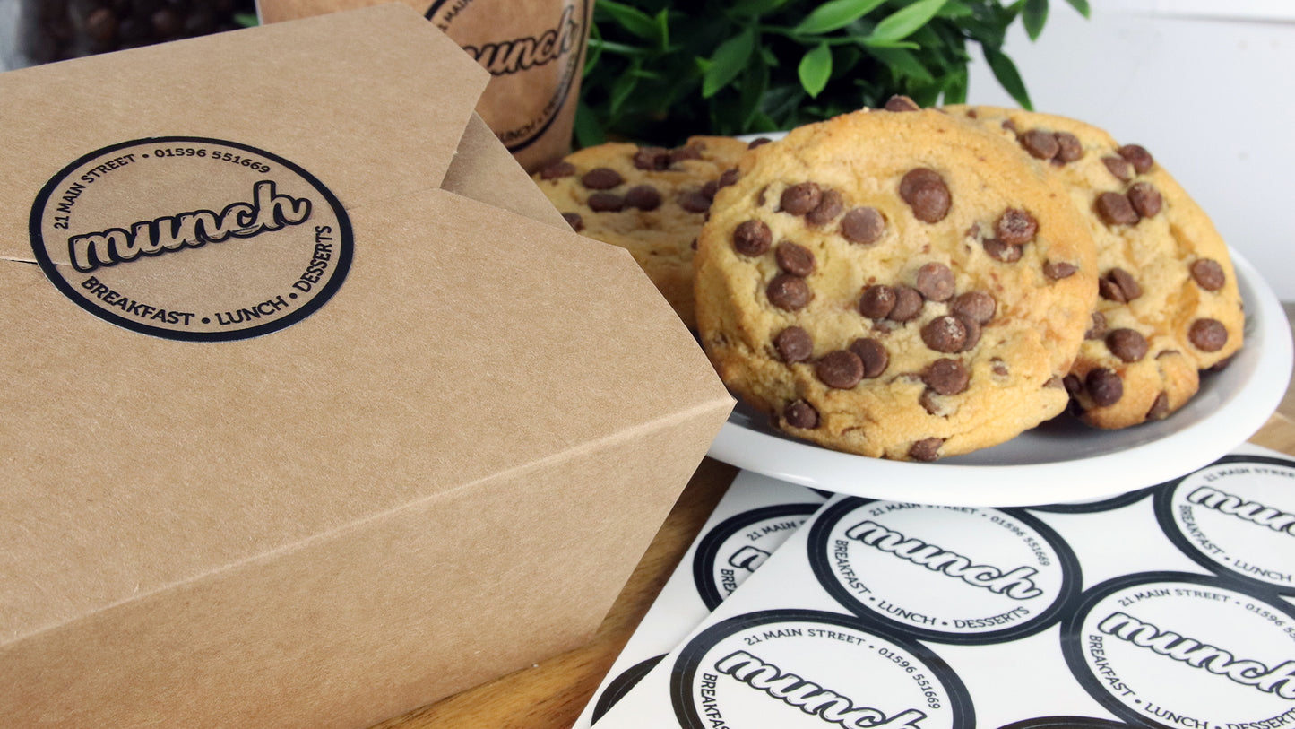 Clear eco friendly compostable labels with munch design applied to a food container and a cardboard coffee cup
