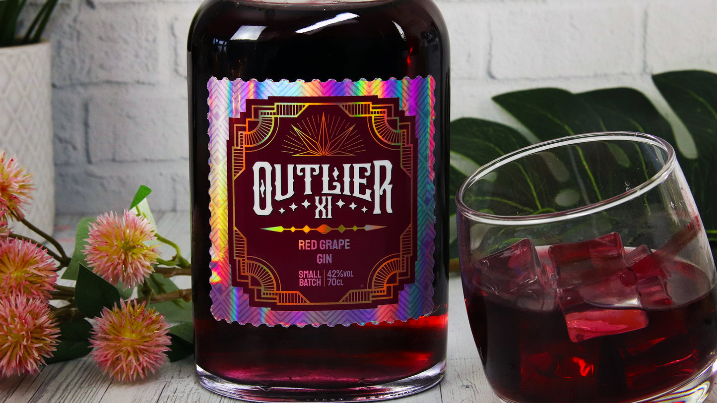Die cut holographic branding label with gin logo to applied to a bottle next to a tilted glass