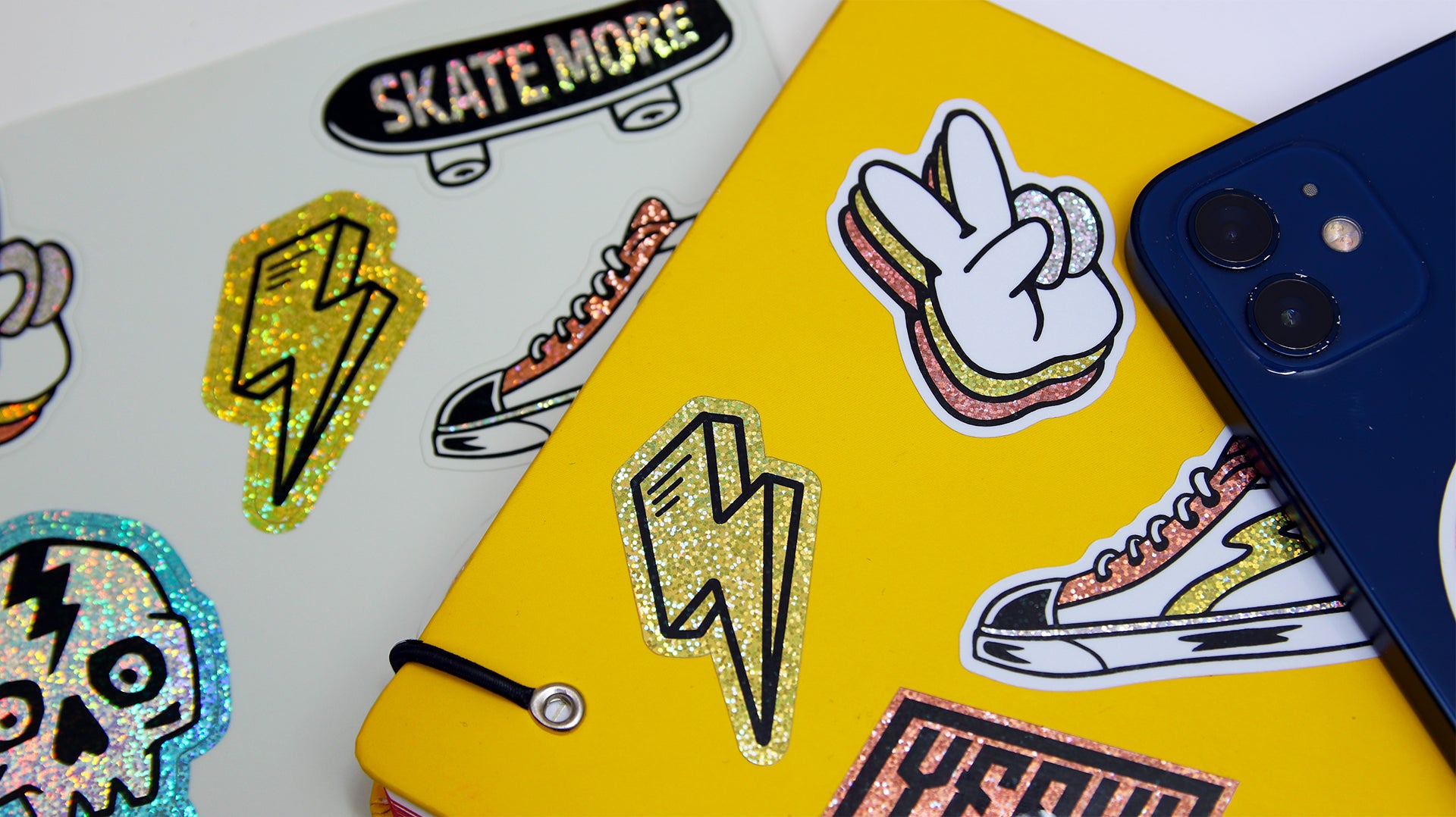 A die cut eco-friendly glitter sticker sheet with various designs, some applied to a yellow notebook