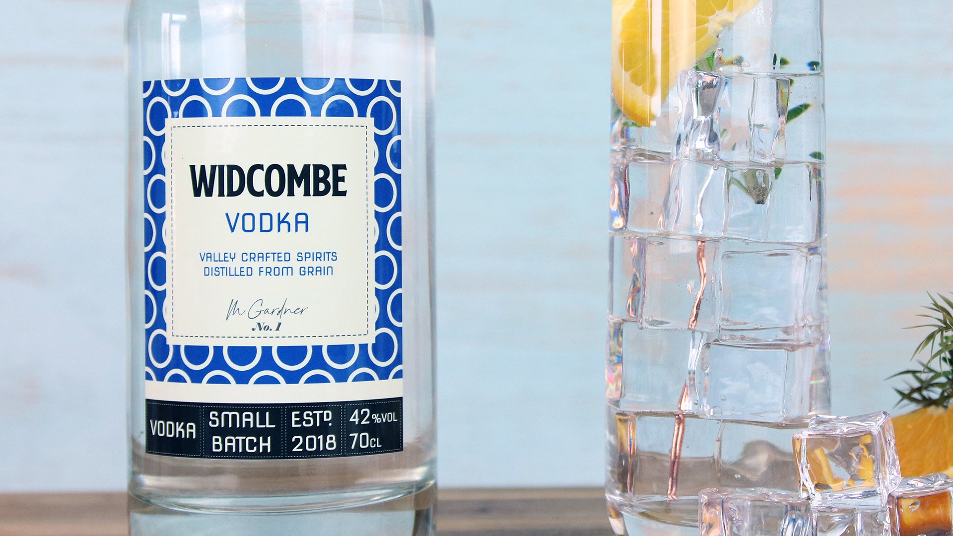 Glass label applied to glass vodka bottle next to long drink glass filled with a cocktail