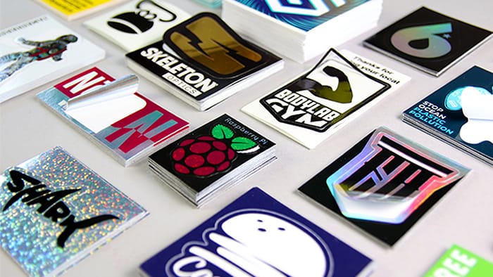 Various kiss cut custom printed stickers in piles with some semi-peeled from their background, all on a grey background