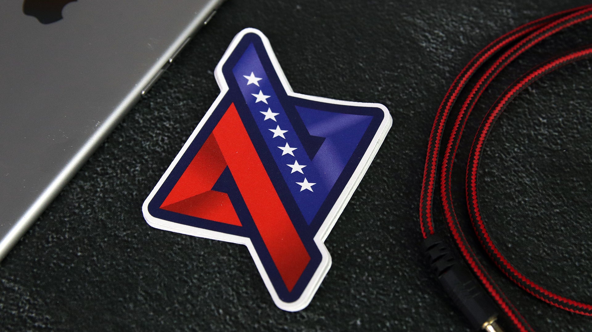 Die cut logo sticker with flag design on a black desk next to a silver iPad