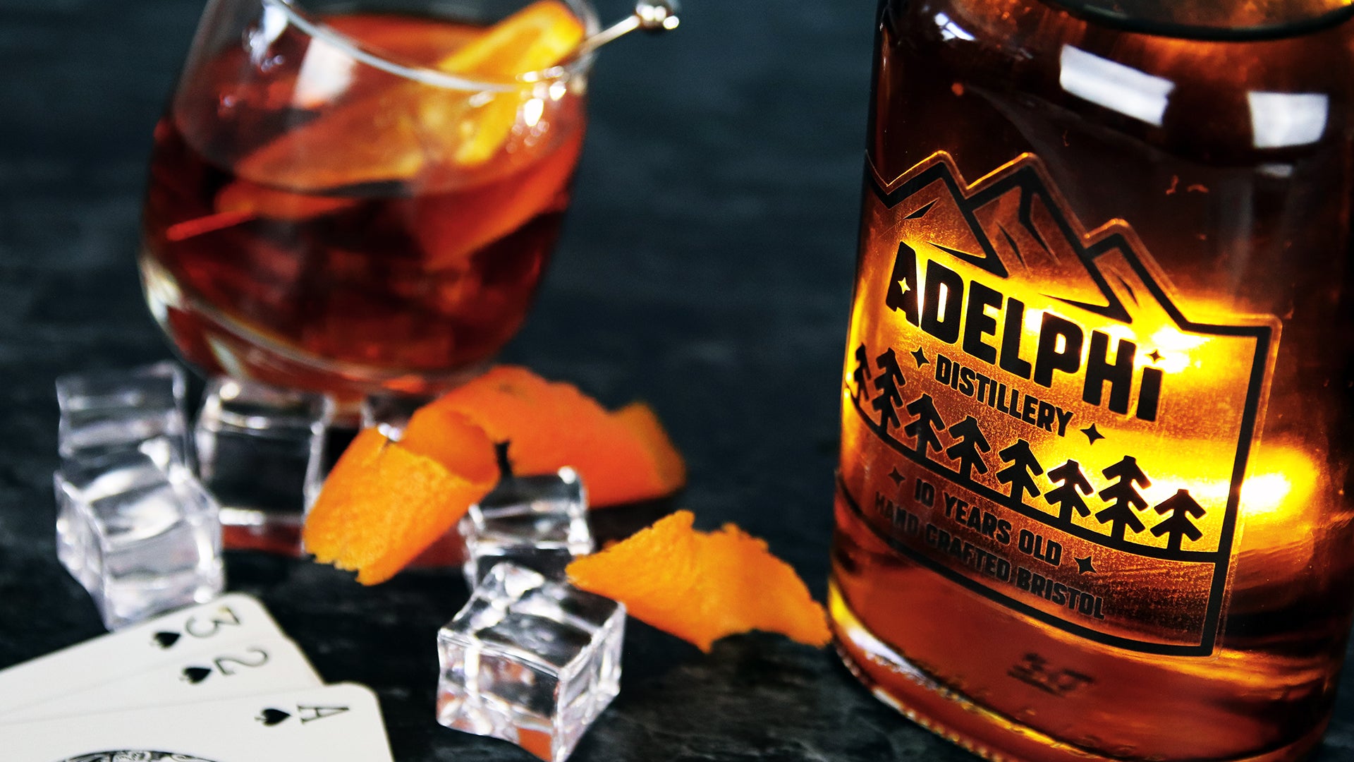 Die-cut transparent label applied to a whisky bottle next to a filled jar orange peel ice cubes and cards