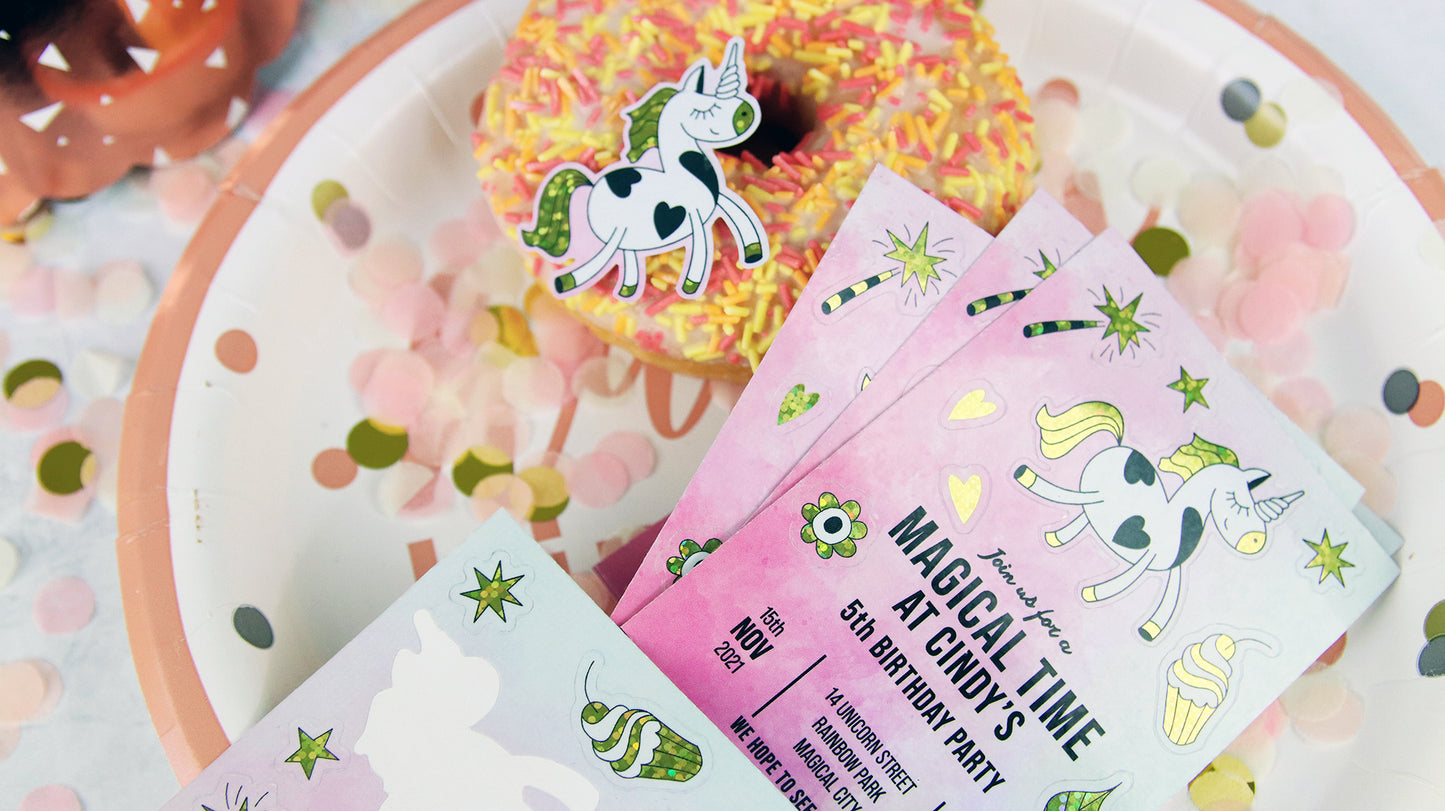 Glitter label birthday invitation with cute peelable sticker designs on a decorated table next to a donut