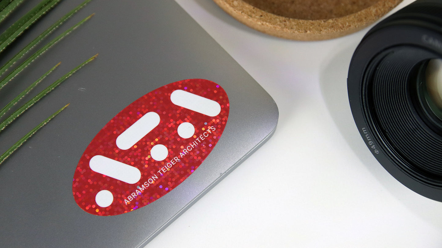 Oval glitter sticker with red ATA logo applied to a silver laptop
