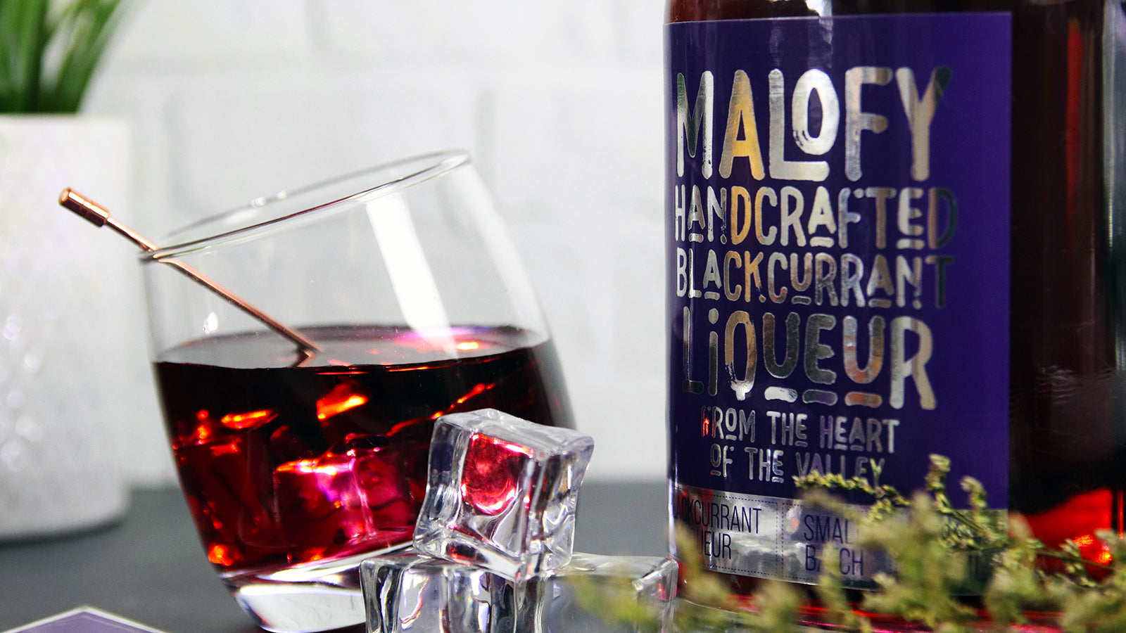 Rectangle mirror silver sticker on a glass bottle containing blackcurrant liqueur next to a tilted glass