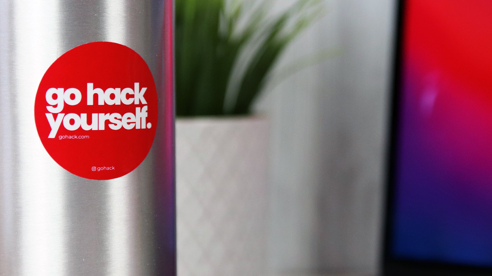 Round white vinyl sticker with go hack yourself design applied to a stainless steel water bottle