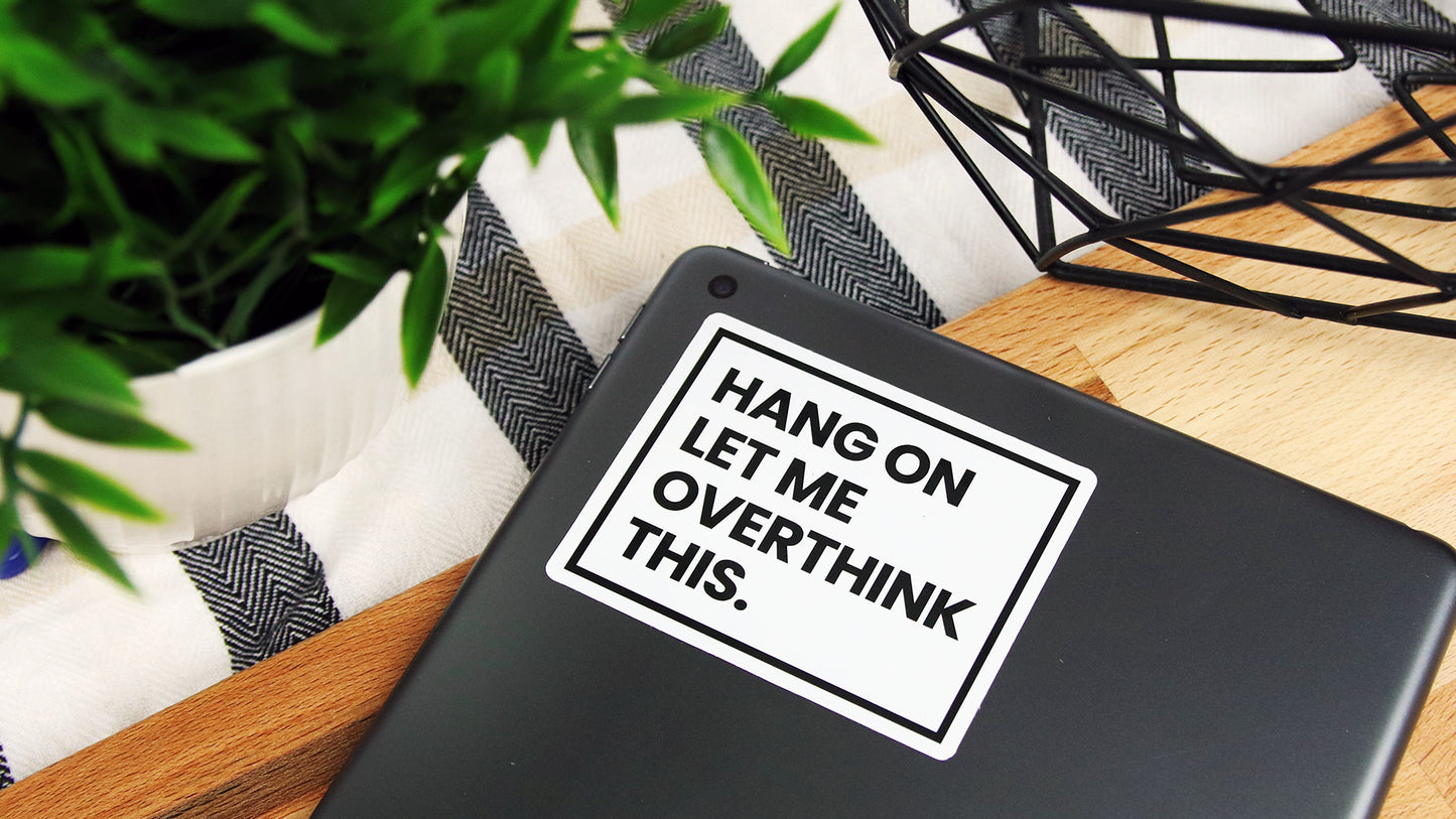 Rounded corner white vinyl sticker with overthink design applied to an iPhone on a table