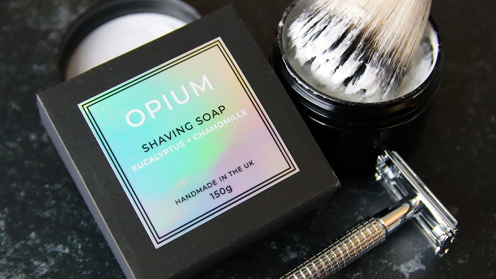 Square holographic sticker applied to black soap box next to shaving tools