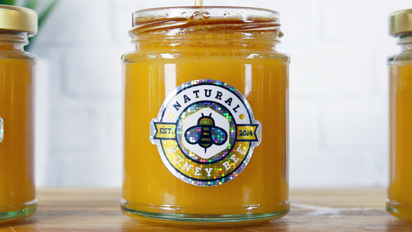 Three die cut glitter jar labels applied to different honey jars on a wooden board