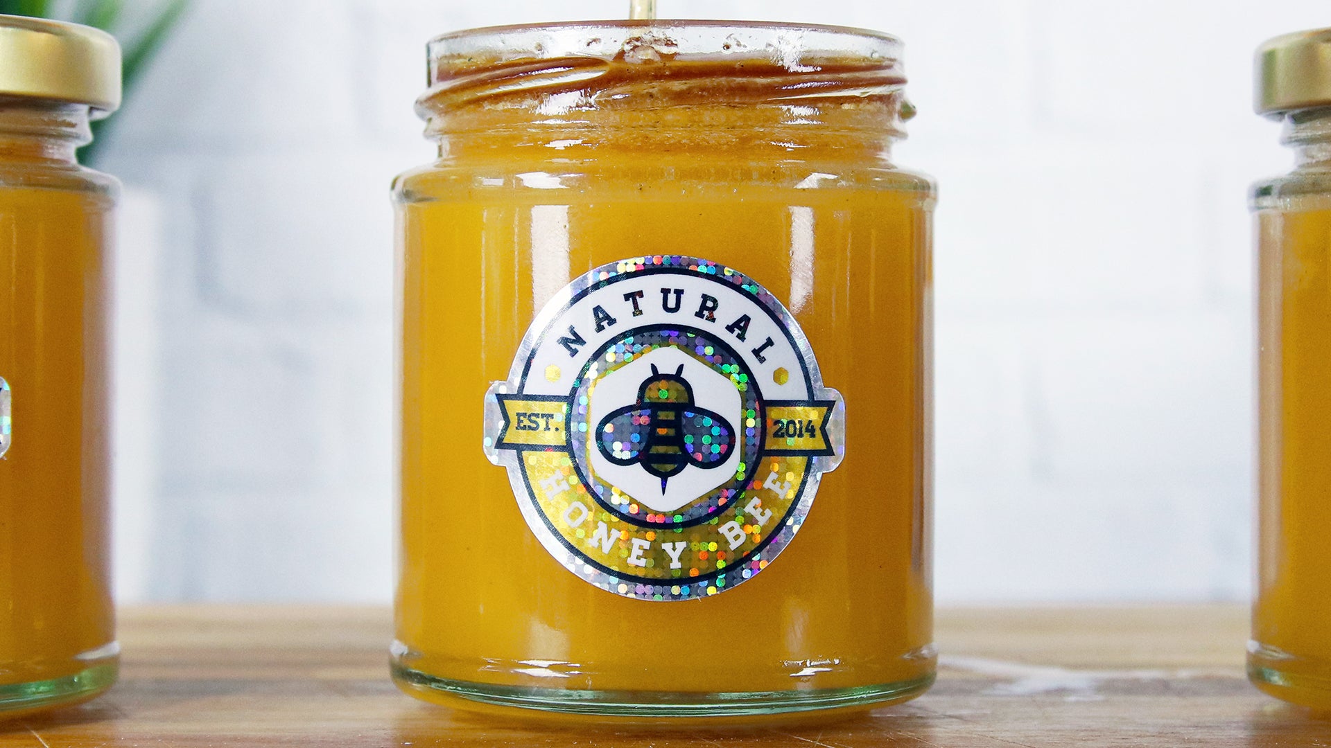 Three die cut glitter stickers applied to different honey jars on a wooden board