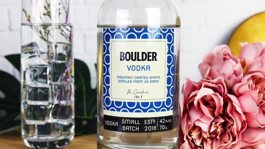 Eco friendly sticker applied to glass vodka bottle next to long drink glass filled with a cocktail